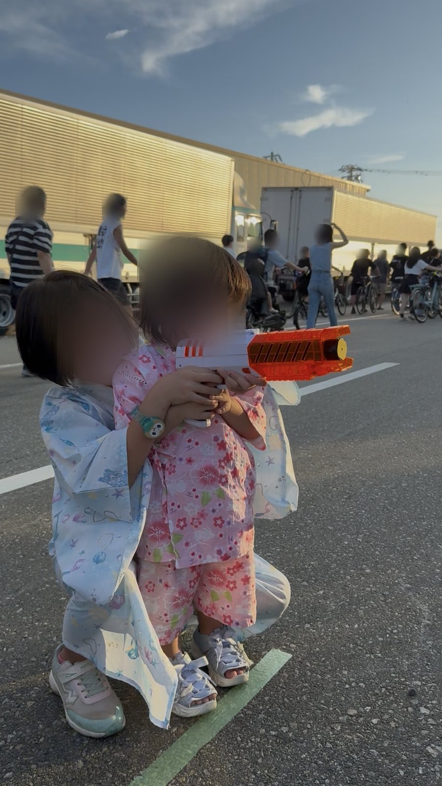 夕暮れの祭り会場で、浴衣姿の子どもがブラスターを構えている様子